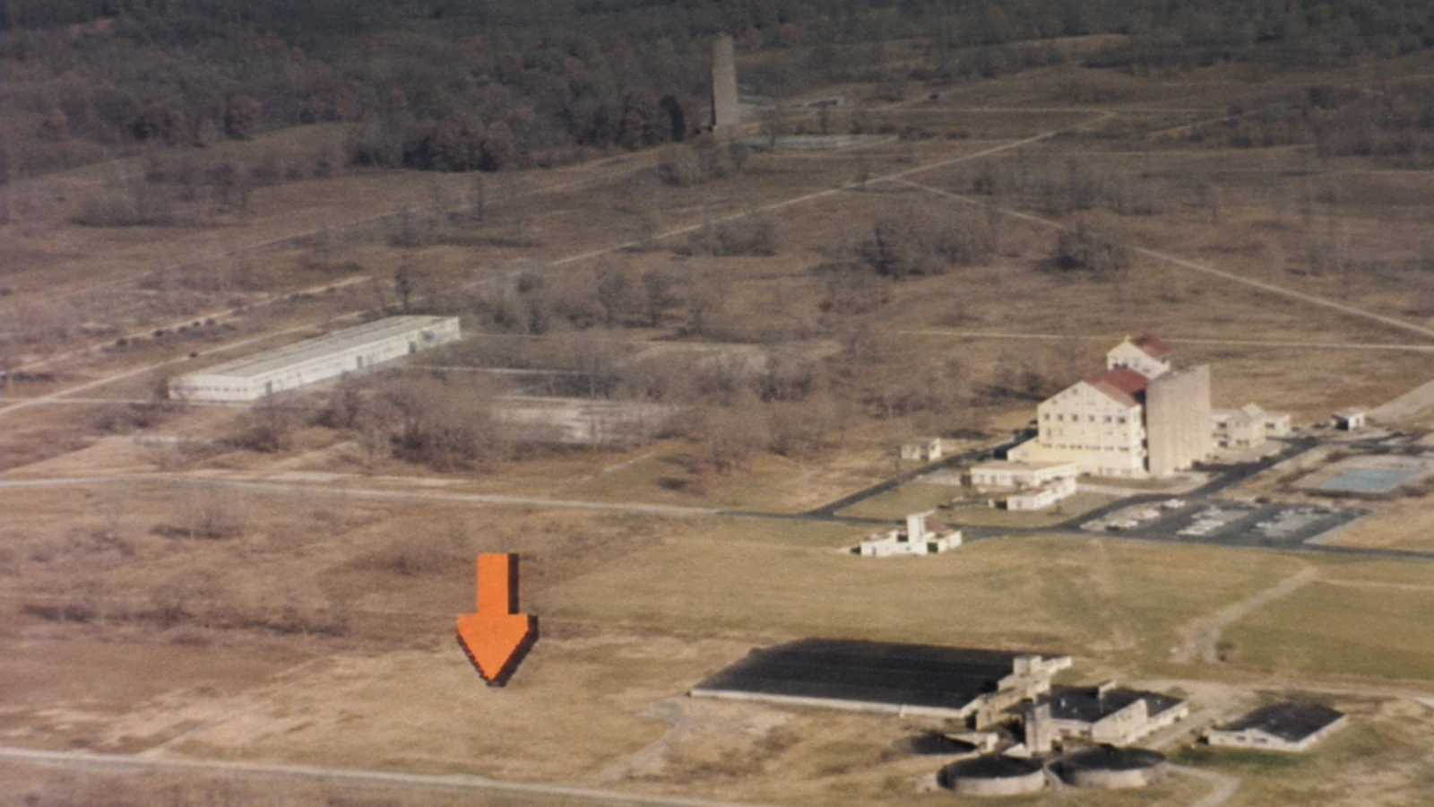 Restored archival aerial frame of the former Lake Ontario Ordnance Works in 1985, with an orange arrow marking an area on the grounds