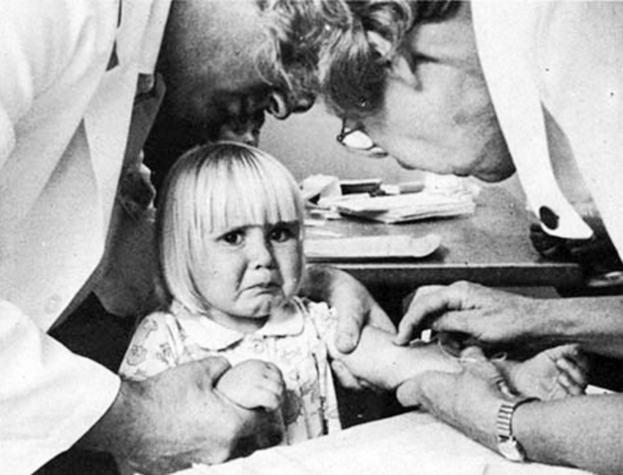 Black-and-white archival photograph of a young child being examined by medical workers